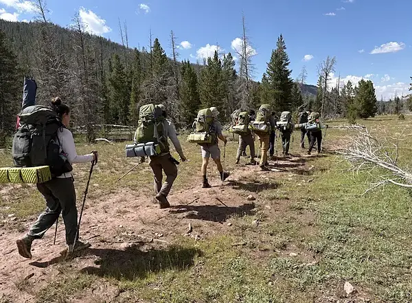 WONDER LSSP 10: Group of hikers with large backpacks walk along a dirt path through a dry, wooded area.