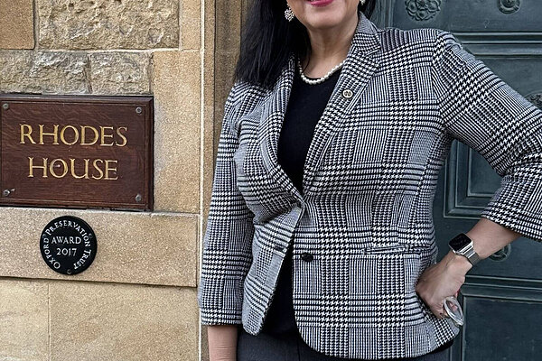 Woman smiles in black and white plaid jacket outside Rhodes House.